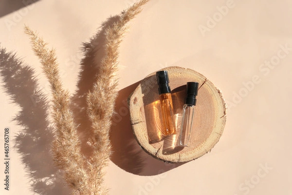 Fototapeta Two glass perfume samples with transparent brown liquid on wooden tray lying on beige background with pampas grass. Luxury and natural cosmetics presentation. Testers on woodcut in sunlight. Top view