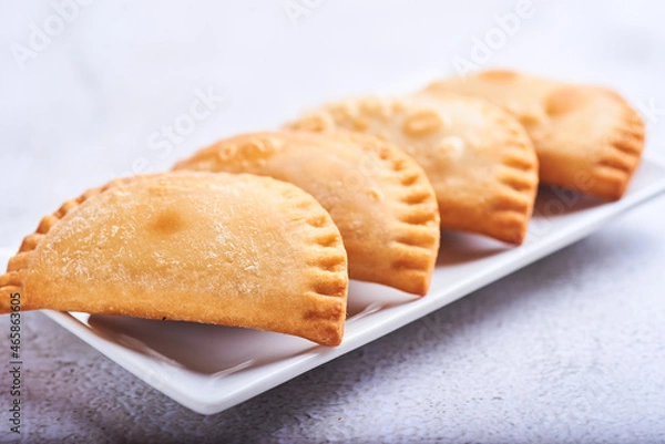 Fototapeta Empanadillas rellenas de atun con tomate y cebolla sobre un fondo blanco.