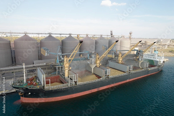 Fototapeta Loading grain into holds of sea cargo vessel through an automatic line in seaport from silos of grain storage. Bunkering of dry cargo ship with grain