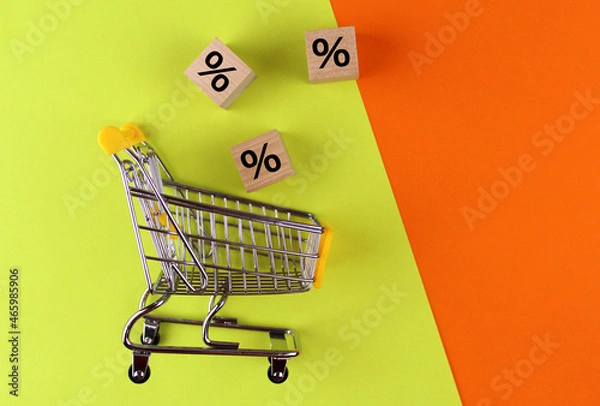 Fototapeta Empty shopping cart with wooden cubes with percent on orange and yellow background