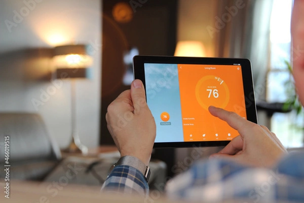 Fototapeta Man is Adjusting a  temperature using a tablet with smart home app in modern living room