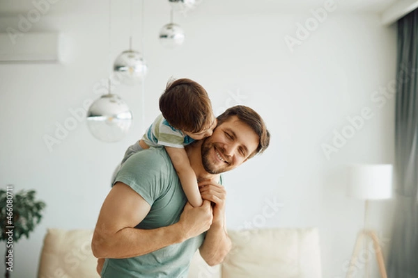 Fototapeta Little boy kisses his father who is piggybacking him while spending time together at home.