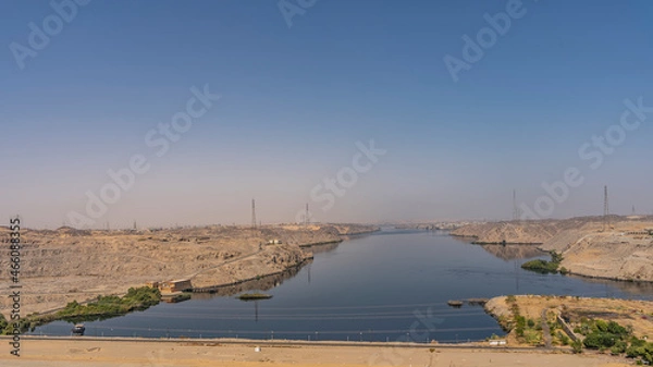 Fototapeta The Nile River in the area of the Aswan Dam. View from the motorway. Technical buildings are visible on the sandy shores. Reflection in blue water. A sunny summer day. Egypt