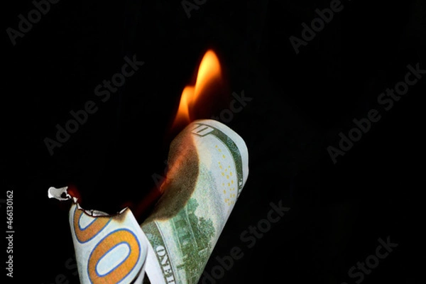 Fototapeta A hundred dollar bill in American US currency is on fire on a black background