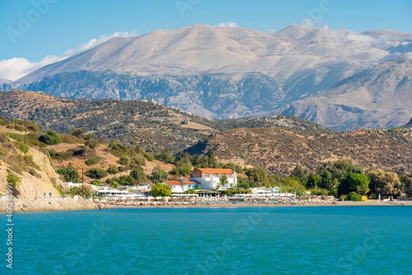 Fototapeta Wind-protected beach and bay with sun loungers and umbrellas in the popular tourist resort of Agia Galini in the south of Crete. In the background the IDA mountain range with the mighty Psiloritis