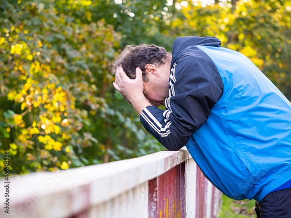 Fototapeta Man with his head in his hands and leaning on the railing, worried and sad