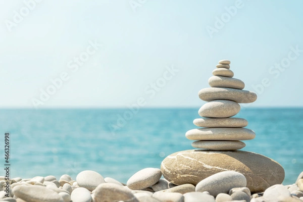 Fototapeta Balanced stack of pebbles on sea beach on sunny day. Natural summer harmony concept with stone pyramid on the coast.