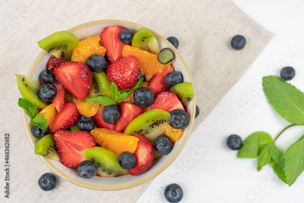 Fototapeta Fresh chopped fruit salad in a bowl on white  background. Top view.