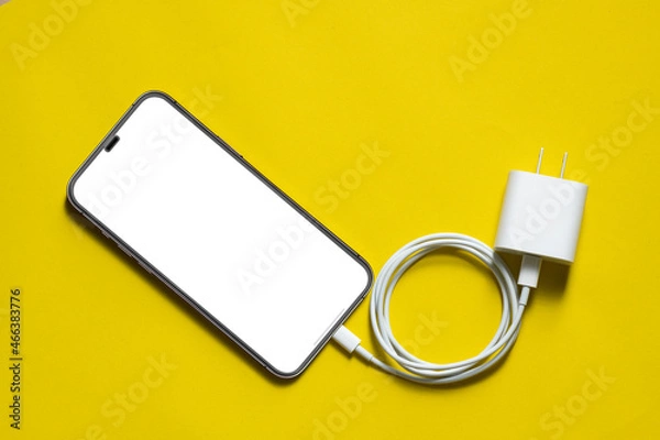 Fototapeta smartphone connects to charger through USB type C cable on yellow background, Top View