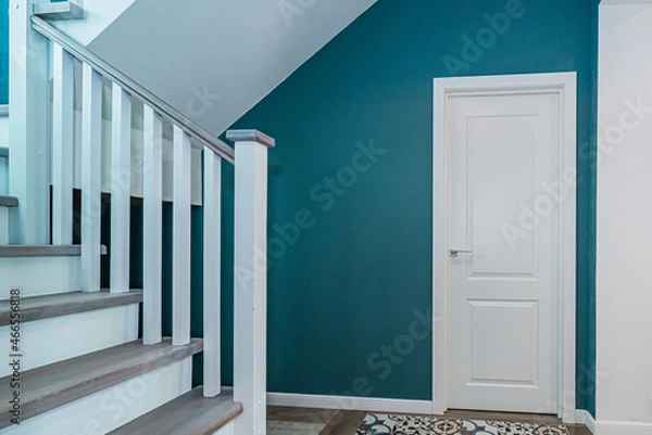 Fototapeta Fragment of a room with a white door, turquoise walls and a wooden staircase