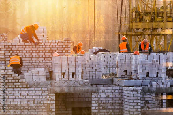 Fototapeta Bricklayer group workers installing brick masonry on exterior wall. Professional construction worker laying bricks. construction site at sunset