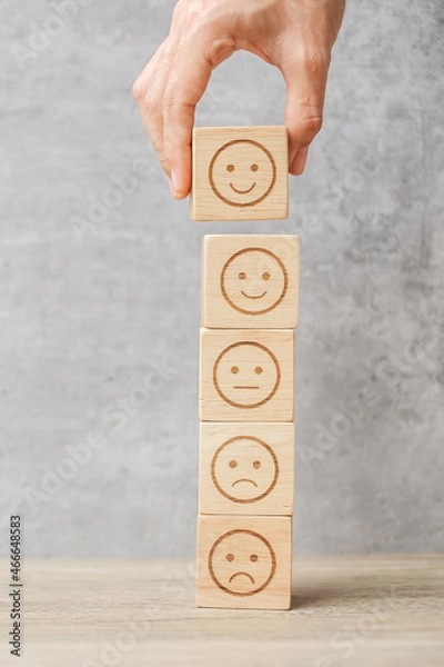 Fototapeta Man hand holding emotion face block. Customer choose Emoticon for user reviews. Service rating, ranking, customer review, satisfaction, mood, evaluation and feedback concept