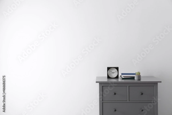 Obraz Books, houseplant and clock on chest of drawers near white wall indoors, space for text. Interior design