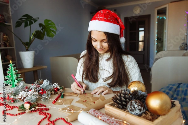 Obraz a smiling girl in a Christmas hat makes an advent calendar