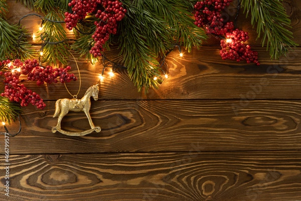 Fototapeta Christmas background. Nobilis fir branches, twigs with red berries, toy golden horse on brown wooden planks. Copy space, flat lay, top view. Holiday, Xmas, New Year concept. Mockup