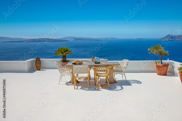 Fototapeta Beautiful Santorini landscape with white architecture and sea view. Sunny summer travel luxury background, cityscape, urban scenic. Idyllic streets, pathway table and chairs as decoration, caldera
