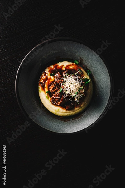 Fototapeta Stewed veal cheeks with mashed potatoes on plate on rustic wooden table dark background