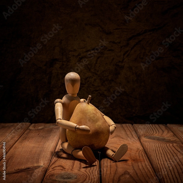 Fototapeta Wooden man gestalta sitting with a yellow pear on a wooden table and art background