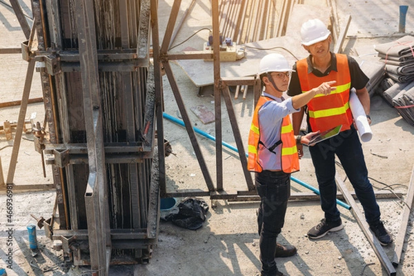 Fototapeta Structural engineer and foreman worker with blueprints discuss, plan inspecting for the outdoors building construction site.