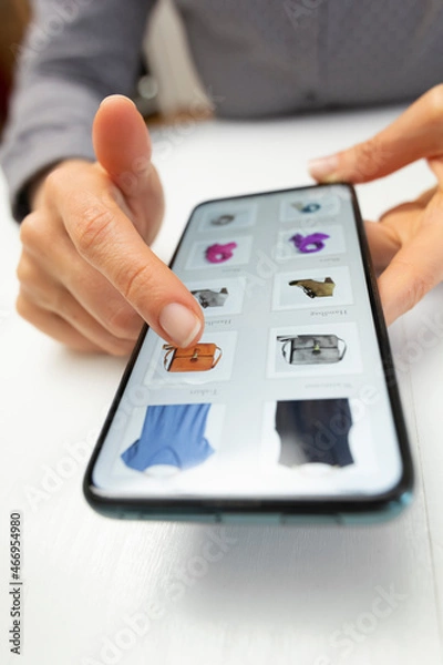 Fototapeta Shopping for clothes in online stores using a mobile phone. Hands of a woman choosing a product on a smartphone screen. E-commerce.	