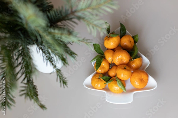 Fototapeta Small ripe tangerines with leaves, on plate in shape of Christmas tree on beige background. Concept winter vitamin food. Moody still life festive composition. For greeting card, book, stories