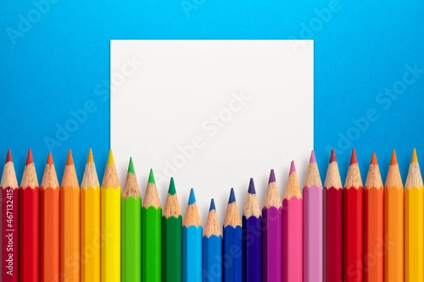 Fototapeta Creative layout made of color pencils on blue paper background with white paper card note. Flat lay. Education concept.