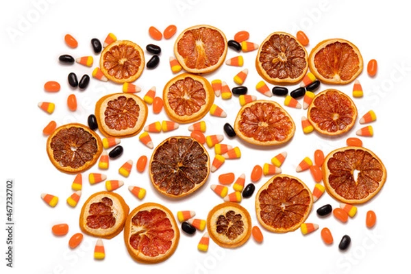 Obraz Flat lay pattern of dried orange slices, candy corn, and black jelly beans on a white background.