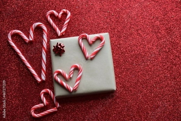 Fototapeta Christmas background. Wrapped present with red bow and five candy cane hearts on red glitter background.