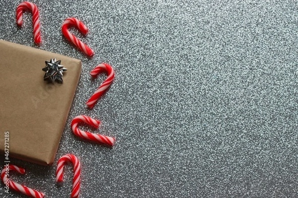Fototapeta Christmas background. Wrapped present with silver bow surrounded by red and white candy canes on silver glitter background.
