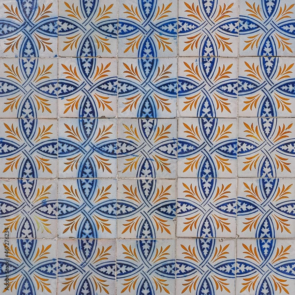 Fototapeta Abstract ornamental background. Fragment of old building wall, with ornate glazed tiles. White tiles with blue orange painted decorations. Azulejos, traditional Portuguese art, for architecture design