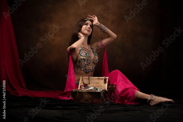 Obraz A girl in the image of an oriental princess is sitting next to a treasure chest. Oriental fairy tale, belly dance, Scheherazade.