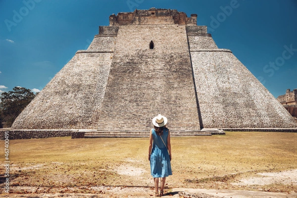 Fototapeta A young woman stands against the backdrop of the Mayan pyramid in Uxmal and enjoys the breathtaking view, from the back. Pyramid of in the ruins of Uxmal, Yucatan, Mexico,Unesco archaeological site