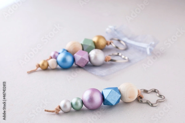 Fototapeta Selective approach of painted wooden bead key chains for car or bag on light background. Wooden beads and hexagon in pink, green, blue and gold metallic colors. Crafts concept...