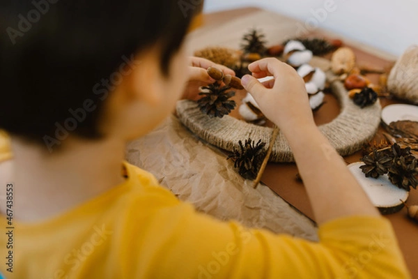 Fototapeta The boy makes a wreath from natural materials. Autumn needlework with handmade children
