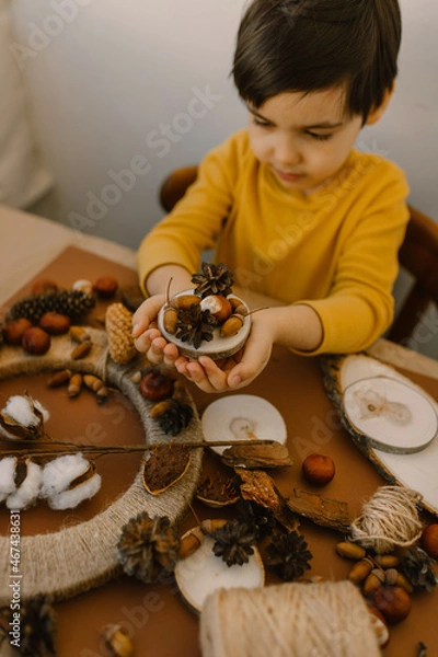 Fototapeta The boy makes a wreath from natural materials. Autumn needlework with handmade children