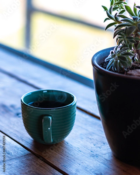 Fototapeta Vertical view of a steaming cup of coffee on a wooden table and a succulent plant on the right.