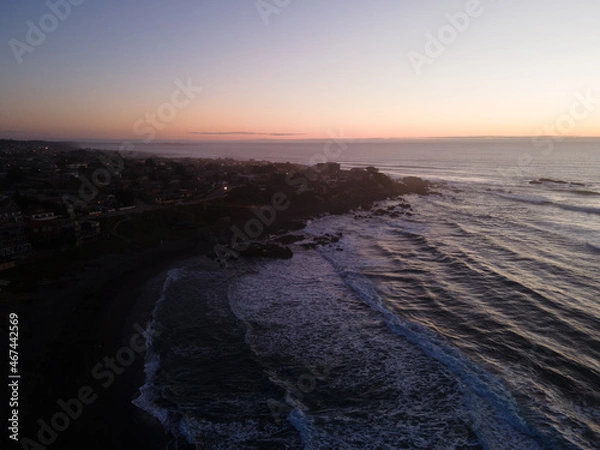 Fototapeta Aerial view of pichilemu being darkened with the sunset in the background.