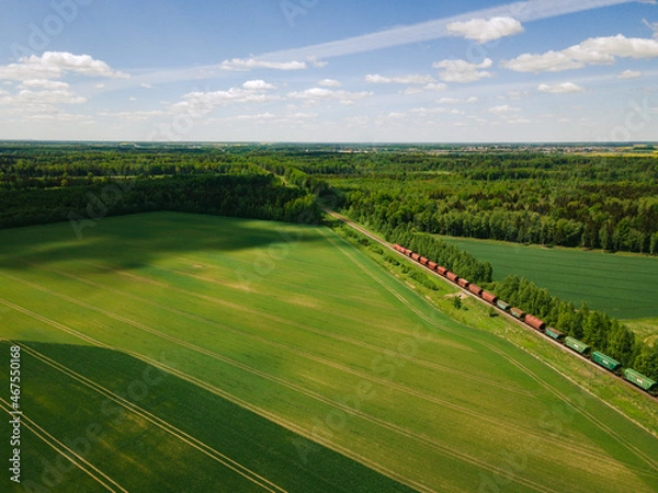 Fototapeta Freight train heading to the green forest in summer from above. Fields and crops. 