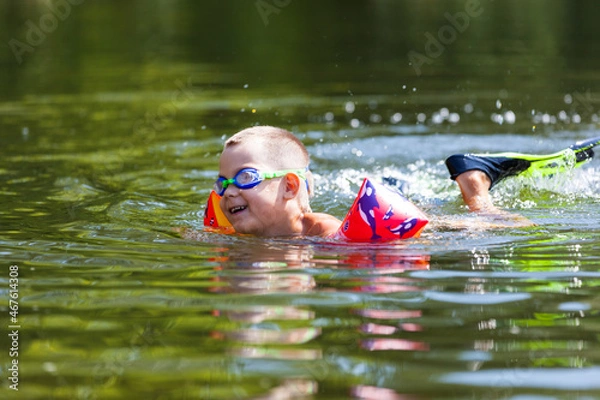 Obraz Cute boy is swimming in the small river with his armbands and goggles