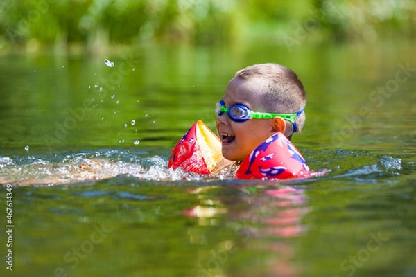 Fototapeta Cute boy is swimming in the small river with his armbands and goggles