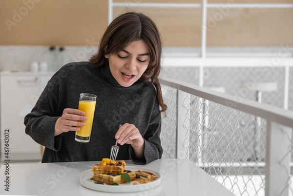 Fototapeta A woman is having breakfast with Belgian waffles and orange juice.