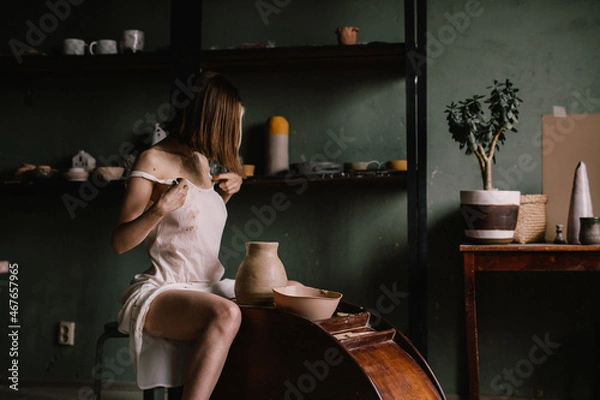 Fototapeta talented sculptor girl in thin light negligee sculpts a jug of clay in pottery workshop near large window. Concept art of sculpture