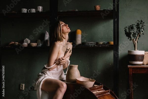 Fototapeta talented sculptor girl in thin light negligee sculpts a jug of clay in pottery workshop near large window. Concept art of sculpture