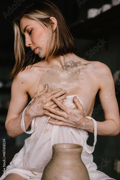Fototapeta talented sculptor girl in thin light negligee sculpts a jug of clay in pottery workshop near large window. Concept art of sculpture