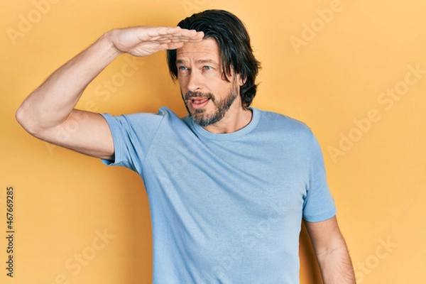 Fototapeta Middle age caucasian man wearing casual clothes very happy and smiling looking far away with hand over head. searching concept.
