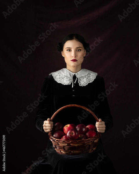 Fototapeta Model in gothic costume on a black background. The girl is holding a red apple as symbol of temptation