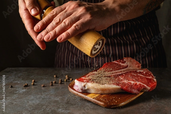 Fototapeta The hands of the chef add fresh pepper from the mill to the beef steak