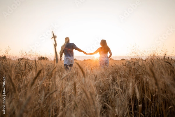 Obraz Mixed race young adult couple holding hands while walking in field