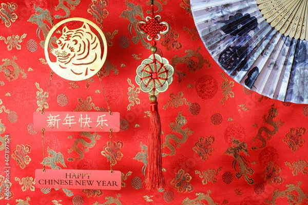 Fototapeta Golden chinese tiger symbol, chinese bamboo paper fan and fortune hunger from lucky coins on red fabric with birds and dragons. Chinese New Year of the Tiger 2022. Translation: happy new year
