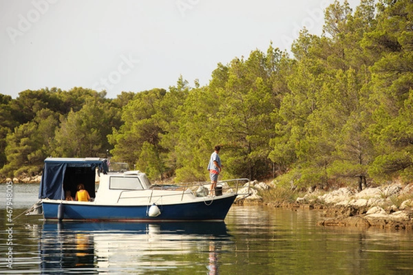 Fototapeta A family on a motor boat moored to the shore of a picturesque bay with a pine forest. Rest at nature. Fishing from a boat. Relax on weekends. Vacation in nature in the water element. Sunny warm summer